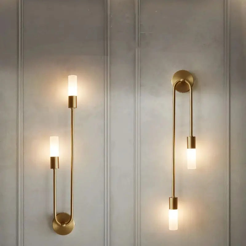 Two gold wall lights mounted on white walls, showcasing a minimalist design for a bathroom sconce.