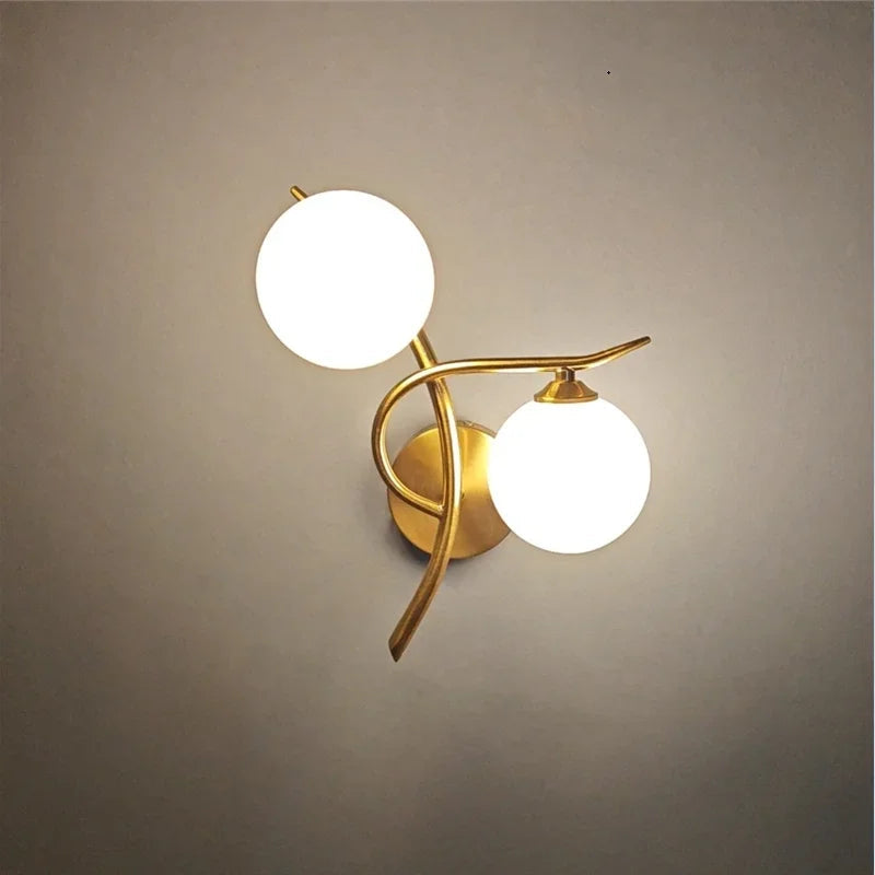 Contemporary 2-globe LED bathroom wall sconce with gold curved arms and frosted glass globes, offering soft ambient lighting for modern interiors.