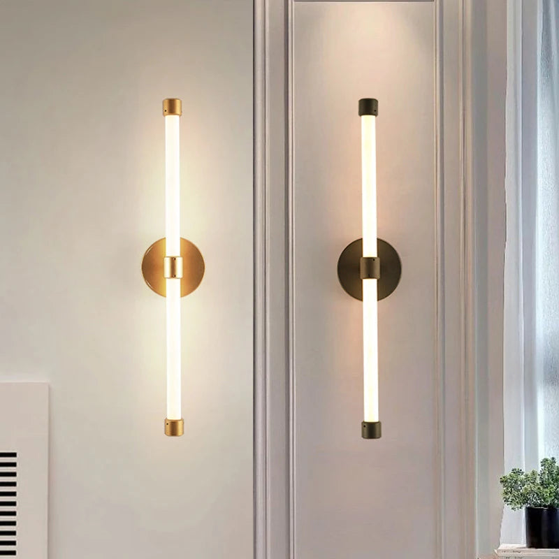 Minimalist modern LED tube wall sconces in brass and black finishes, vertically mounted for elegant hallway or bathroom lighting