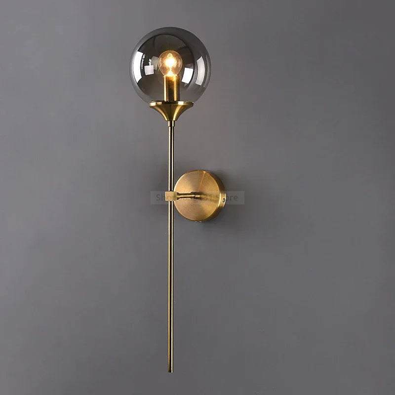 Modern wall sconce with smoky glass globe and brushed gold vertical rod, combining minimalist elegance with ambient lighting for hallways, bedrooms, or bathrooms.