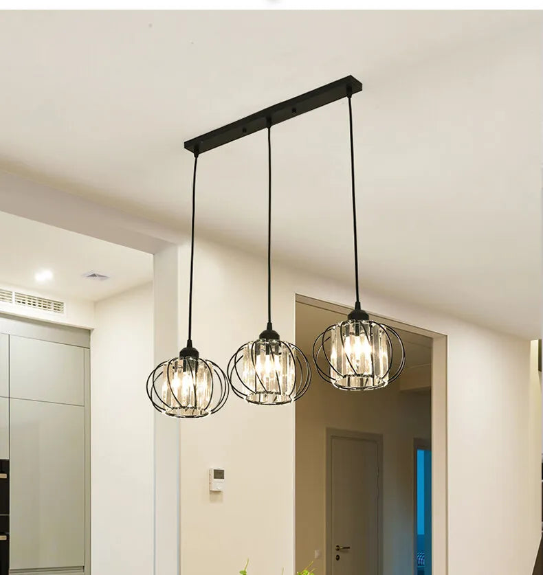 A modern kitchen features a trio of hanging chandeliers, providing a chic and bright atmosphere for cooking and dining.