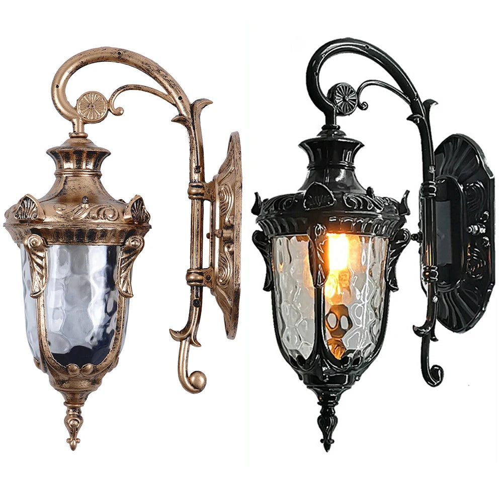 Antique-style outdoor wall lantern with ornate scrollwork arm and textured glass shade in bronze and black finishes, ideal for entryways or garden walls.